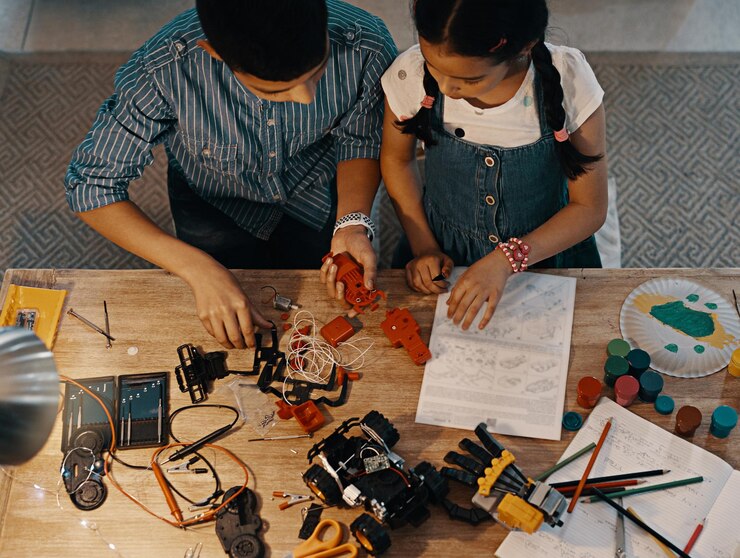 Header image: A child building a small robot with wires, sensors, and LEDs under the guidance of a teacher in a hands-on STEM workshop