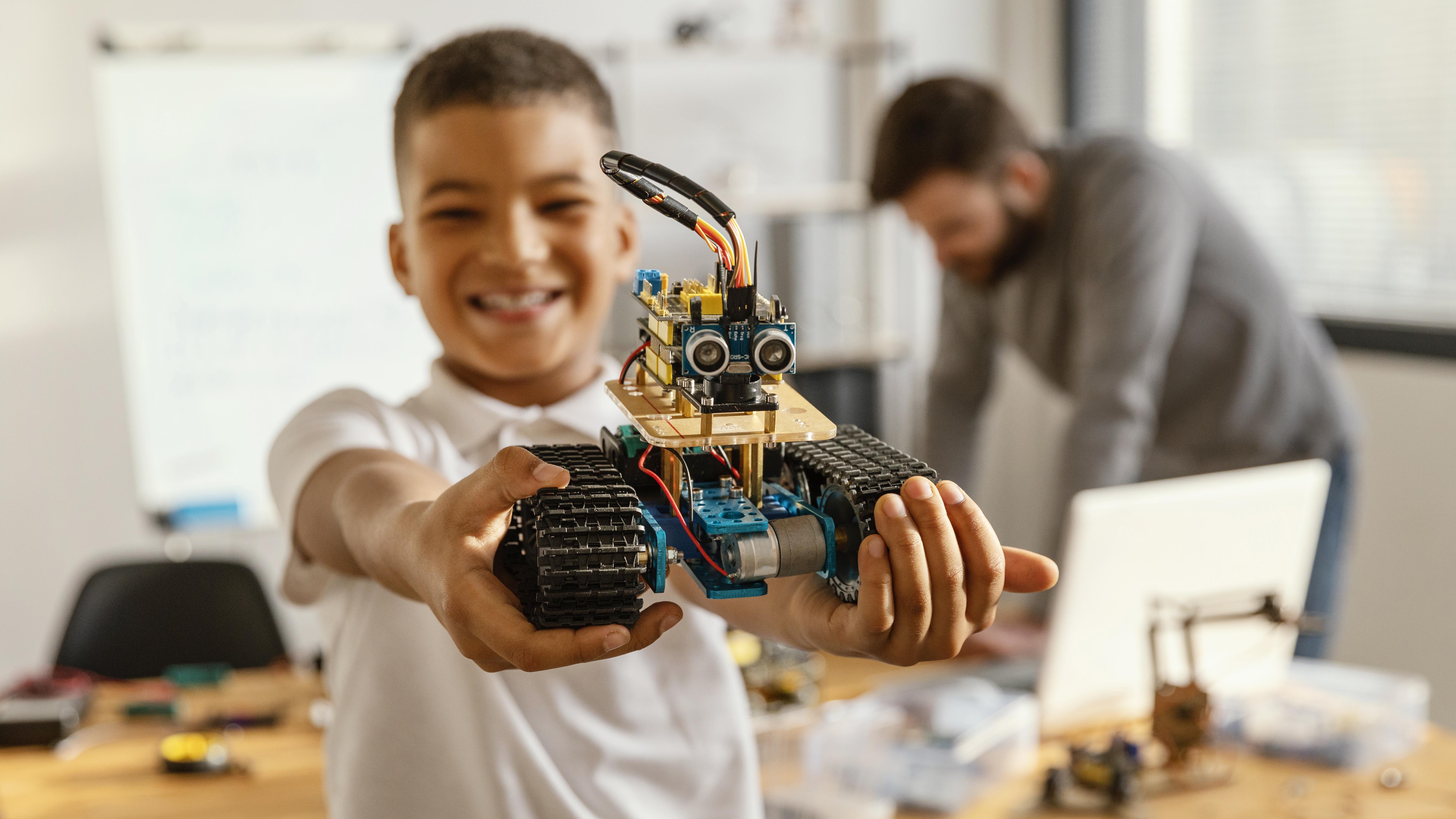 Header image: Student proudly holding a small robot they built